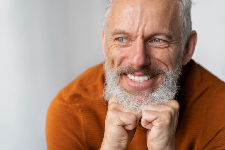 Homem sênior sorridente com barba grisalha e dentes saudáveis após implante dentário na Odonto Caprio.