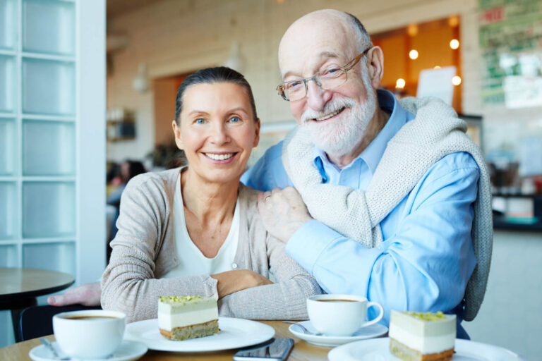 Casal de idosos sorrindo felizes em um café após tratamento seguro de implante dentário no Brooklin com a equipe da Odonto Caprio.