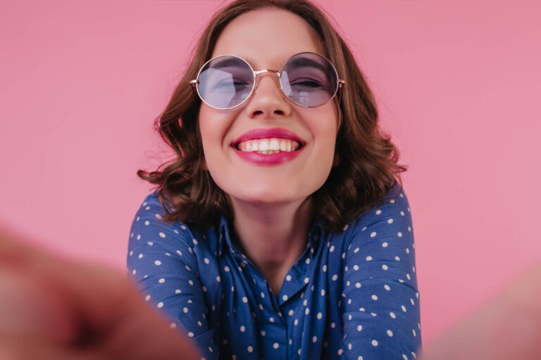 Mulher sorridente de óculos escuros exibindo dentes brancos e alinhados, destacando o resultado de lentes de contato dental no Brooklin.